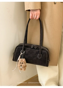 Detail of dark brown leather bowling bag with white stitching and plush dog charm