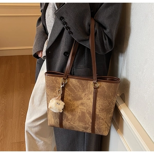 Detail of vintage brown leather tote bag with gold logo and plush eye charm on shoulder