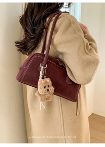 Detail of burgundy retro bowling bag with a cute plush dog pendant on a beige coat