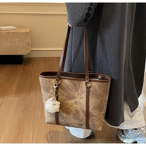 Detail of a brown marble textured tote bag with metal ring and plush charm accessory