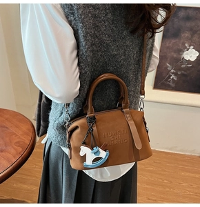 Dettaglio borsa Boston in pelle marrone con testo goffrato e ciondolo a cavallo