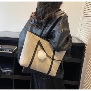 Detail of a large beige marbled tote bag with black leather straps and a plush charm