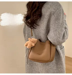 Close-up of brown pebbled leather bucket bag featuring a cute plush bear charm decoration