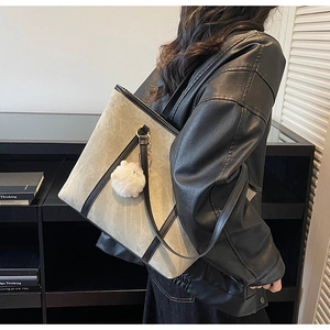 Detail of gray-green matte leather tote bag with black straps and soft fur pompom charm