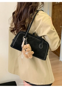 Detail of black vintage bowling bag with white stitching and plush bear charm on model