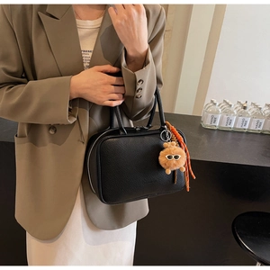 Detail der schwarzen Handtasche aus Narbenleder mit Plüschanhänger und Seilakzent