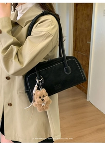 Detail of black suede underarm bag with contrast stitching and plush dog charm accessory