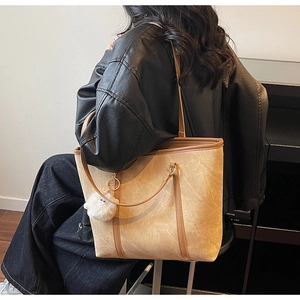 Detail of camel tote bag with retro matte texture, long straps and white plush charm