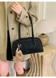 Close-up of black retro bowling bag with white stitching and plush dog charm