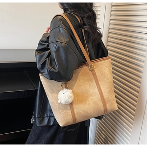 Detail of tan textured faux leather tote bag with slender straps and plush charm