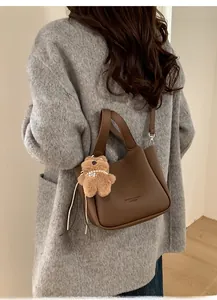 Litchi texture leather bucket bag shown on shoulder with cute plush bear pendant accessory