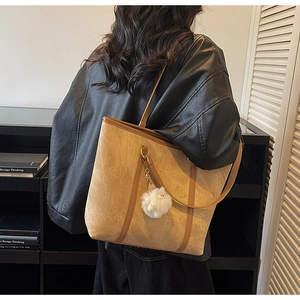 Brown tote bag with dark trim and white fluffy charm worn by a model in a casual setting