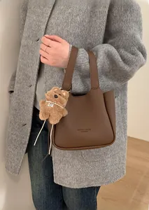 Detail of dark brown grained leather handbag with cute plush bear charm on handle