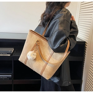 Detail of beige suede tote bag with brown leather handles and plush charm on female model