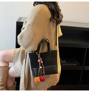 Detail of a black leather crossbody bag with colorful plush ball and bead charms