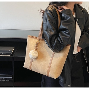 Detail of khaki tote bag with slender brown handles and white plush monster charm