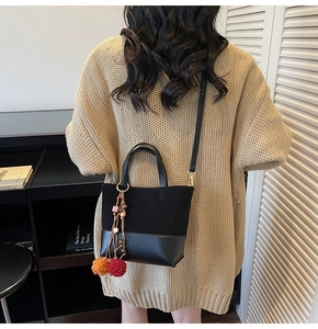 Detail of black vintage bucket bag with decorative colorful pompoms on beige knitwear
