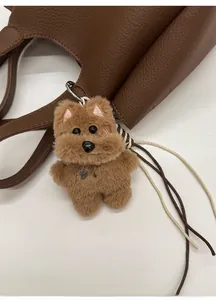 Brown plush dog charm with pearl necklace and bone tag on a textured leather bag