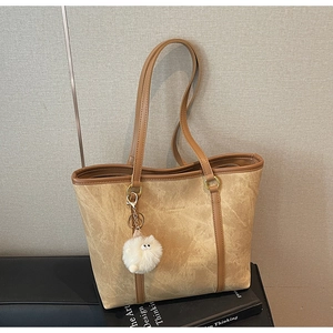 Detail of khaki suede tote bag with stone texture, leather strap and white plush charm