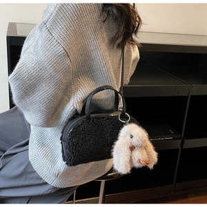 Details einer schwarzen Plüschhandtasche mit lockiger Textur und grauem Hasenanhänger