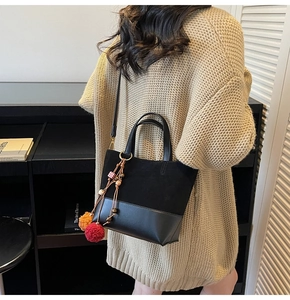Detail of a black bucket bag in suede and leather mix with colorful pom-pom charm