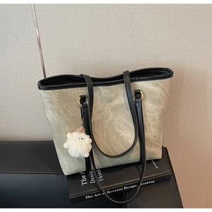Detail of marble pattern suede tote bag with plush charm and black handles on a sofa