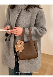 Close-up of retro litchi grain texture on coffee leather bucket bag with bear pendant