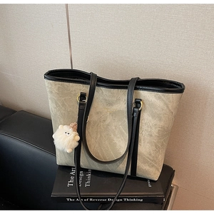 Detail of grey suede tote bag with black handles and cute plush sheep pendant