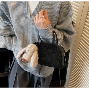 Nahaufnahme einer schwarzen Plüschtasche mit beigem Hasenanhänger und Ledergurt