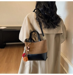 Detail of color-block tote bag with tassel charm worn by model in beige trench coat