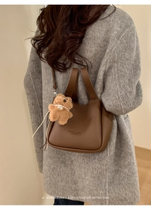 Detail of brown litchi leather bucket bag with cute bear charm worn over a grey coat