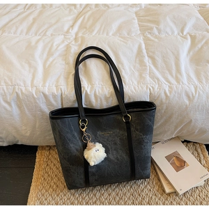 Detail of black marble textured tote bag with golden hardware and white plush keychain