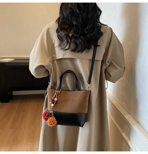 Detail of a brown and black tote bag with plush pom-poms on a trench coat model