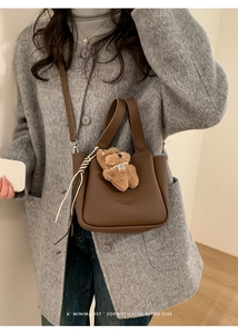 Detail of brown litchi pattern leather bucket bag with cute plush bear charm