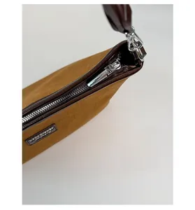 Detail of brown suede handbag featuring silver metal zipper and brand logo plaque