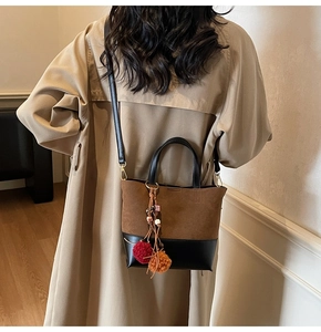 Detail of color-block tote bag with suede texture and decorative plush ball pendant