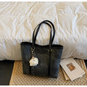 Close-up of dark grey tote bag with marble texture, gold hardware and plush charm