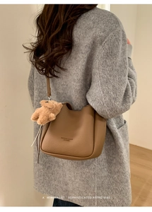 Close-up of brown lychee grain bucket bag with a cute plush bear pendant on a grey coat