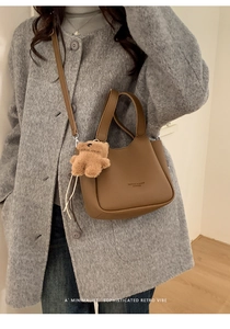 Detail of dark brown leather bucket bag with plush bear charm and minimalist text