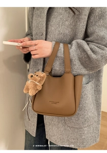 Detailed view of a brown pebbled leather bucket bag with a cute teddy bear pendant charm
