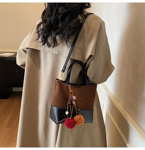 Detail of a vintage contrast bucket bag with pompom charm on a beige trench coat