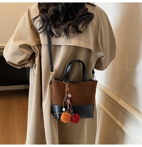 Detail view of a color-block bucket bag with suede texture and decorative pom-pom charms