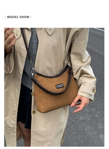 Detail of a caramel suede crescent shoulder bag with a black logo patch and adjustable strap