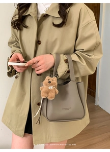 Detail view of grey lychee grain leather bucket bag with a cute plush bear charm