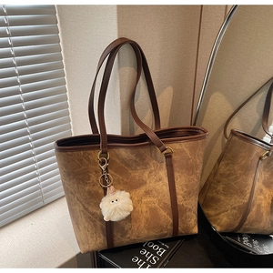 Detail of vintage brown marbled tote bag with cute white plush charm in soft sunlight