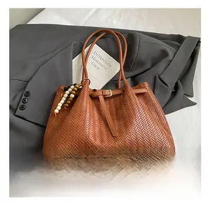 Close-up of brown woven tote bag with bead pendant on a dark grey blazer