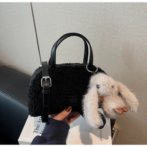 Detail der schwarzen Plüschhandtasche mit süßem beigem Hasenanhänger und Ledergriff