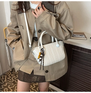 Details der weißen Eimertasche mit Webmuster und dekorativem Holzperlen-Anhänger