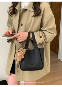 Detail of black pebbled leather bucket bag featuring a brown plush puppy charm pendant