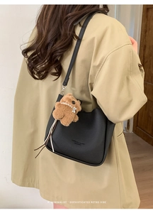Close-up of black litchi grain bucket bag with cute brown plush bear pendant detail